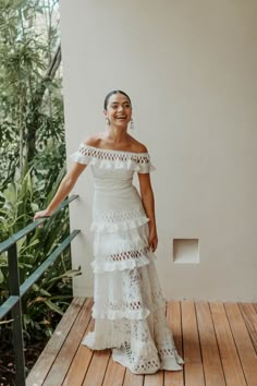 a woman in a white dress is standing on a wooden deck and smiling at the camera