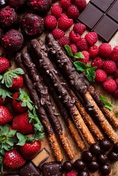 chocolate covered strawberries, raspberries and other fruit on a wooden table next to bars