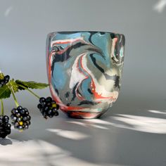 a vase with some blackberries next to it on a white surface and a plant