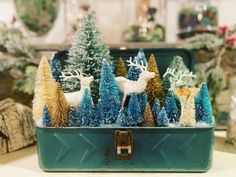 small christmas trees and deer are in a green container on a table with other holiday decorations