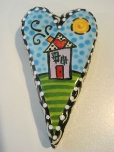 a heart shaped object with a house painted on the front and side, sitting on a white surface