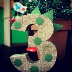 the number three is made out of cardboard and sits next to a potted plant