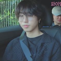 two young men sitting in the back seat of a car, one with glasses on