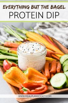 a wooden tray topped with veggies and a jar of protein dip next to it