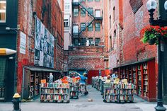 an alleyway filled with lots of books and people walking through it in front of tall brick buildings