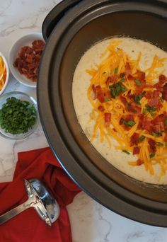 a bowl of soup with cheese, bacon and green onions next to bowls of condiments