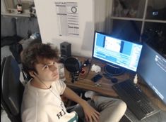 a man sitting in front of a laptop computer on top of a desk next to a monitor