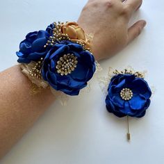 two blue flowers are on the arm of a woman's hand, one is wearing a gold brooch