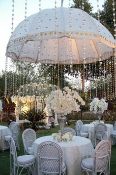 an outdoor dining area with tables, chairs and an umbrella over the table is decorated with white flowers