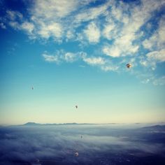 several hot air balloons are flying in the sky above some clouds and land below them