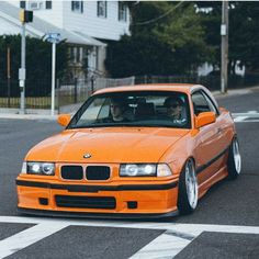 an orange bmw is driving down the street