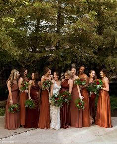 a group of women standing next to each other holding bouquets in front of trees