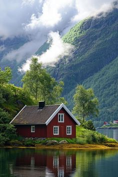 a red house sitting on top of a lush green hillside next to a body of water