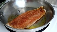 a piece of fish is cooking in a pan on the stove top with oil and seasoning