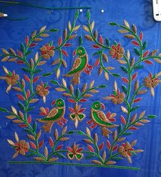 an embroidered piece with birds and flowers on it, sitting on a blue table cloth