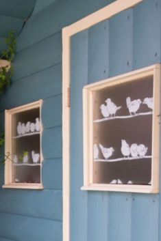 two windows with birds drawn on them in front of a blue house