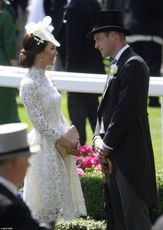 a man and woman standing next to each other in front of a white fence at a horse race