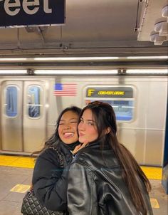 two young women hugging each other in front of a subway train at the station with their arms around each other