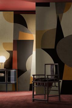 a chair and table in front of a wall with abstract designs on it, next to a lamp