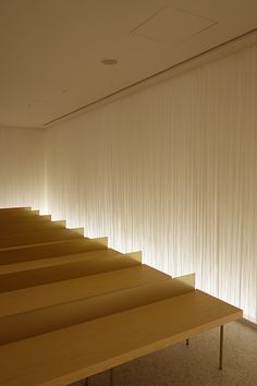 an empty room with white curtains on the wall and wooden table in front of it