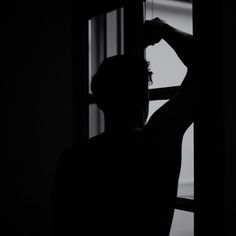 a man standing in front of a window with his hands on his head and looking out the window