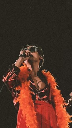 a woman in a red dress singing into a microphone with orange feathers around her neck