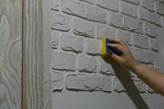 a person using a sponge to paint a brick wall with white bricks and wood grains