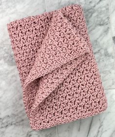 a pink crocheted blanket laying on top of a white marble tile countertop