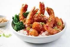 shrimp with broccoli and rice in a white bowl next to a small bowl of sesame seeds