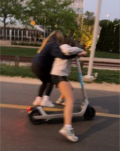 two people riding scooters in the street with their arms around each other's shoulders