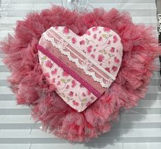 a heart hanging on the wall with pink and red feathers around it's edges