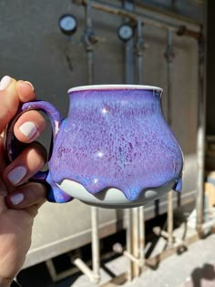 a hand holding a purple and white coffee mug