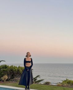 a woman standing on the edge of a swimming pool next to an ocean and trees