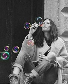 a woman sitting on the ground blowing soap bubbles in front of her face and looking up into the sky