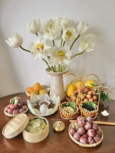 a table topped with bowls and baskets filled with food next to white tulips