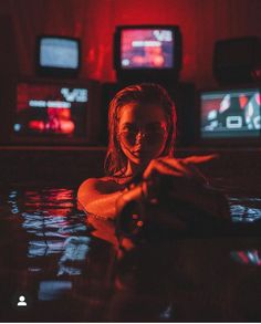 a woman is in the water with her hand up to her face and some televisions behind her