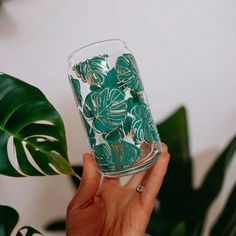 a hand holding a glass with green leaves on it