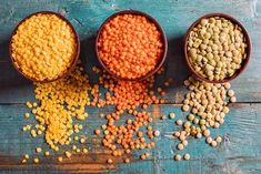 three bowls filled with different colored lentils on top of a blue wooden table next to another bowl