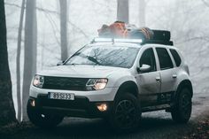 a white truck with luggage on top driving down a road in the foggy woods