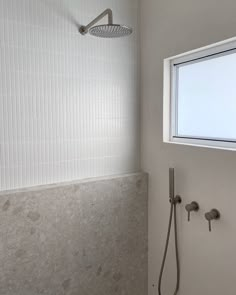 the shower head is next to the window in the bathroom with white tile on the walls