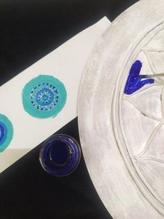 a white plate with blue and green designs on it next to a knife and paintbrush