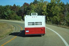 a red and white trailer is driving down the road in front of some trees on both sides