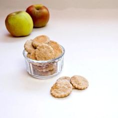 an apple and some cookies in a glass bowl on a table next to two apples