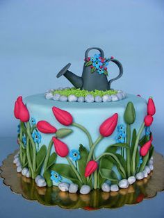 a blue cake with flowers and a watering can on it's frosting surface