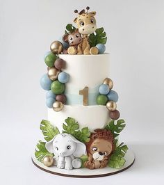 a three tiered cake decorated with animals and jungle leaves on the top, along with balloons