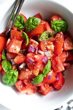 a white bowl filled with sliced tomatoes and green leafy greens on top of a checkered table cloth