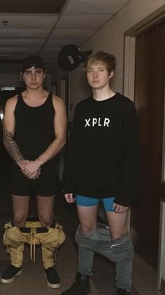 three young men standing next to each other in an office hallway wearing black shirts and blue shorts