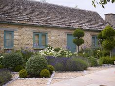 an old stone house with green shutters and blue windows is surrounded by colorful flowers