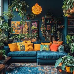 a living room filled with lots of potted plants next to a blue couch covered in yellow and orange pillows