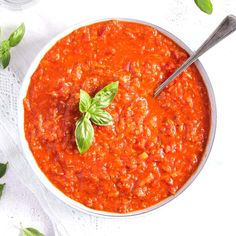 a white bowl filled with tomato sauce and basil leaves on top of a table cloth